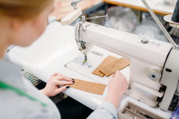 Dressmaker sews fabrics on a sewing machine. Tailoring or dressmaking on clothing factory, needlework, female seamstress in workshop